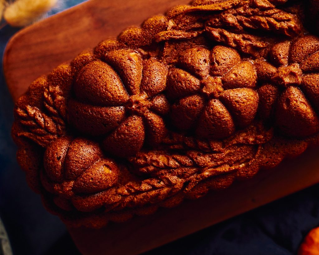pumpkin loaf made with nordicware pumpkin wheat loaf pan on a blue background with cinnamon, pumpkins, forks, plates, and napkins