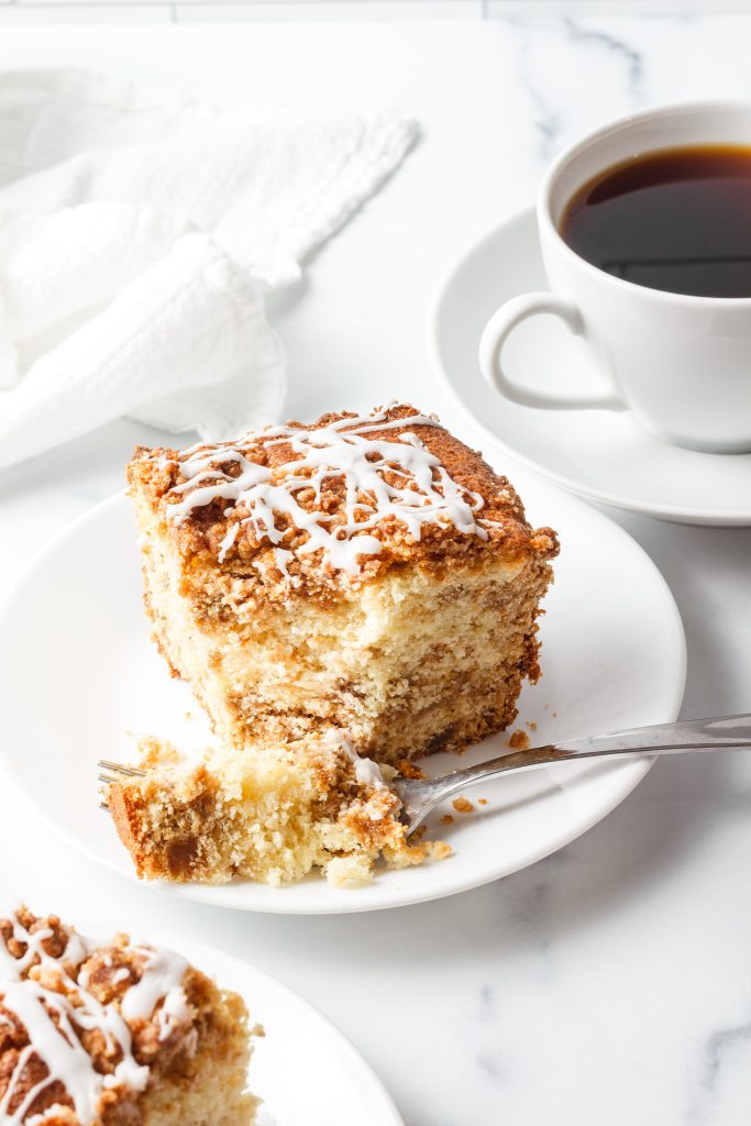 streusel cinnamon coffee cake on a plate with a fork with coffee in the background on a white neutral background