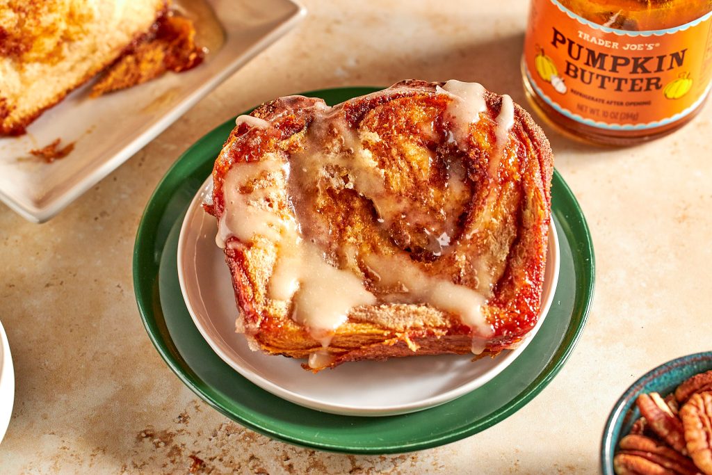 Cinnamon pull apart bread made with biscuits and cinnamon rolls and trader joe's pumpkin butter with a bowl of cinnamon sugar on a neutral background with plates and a pumpkin in the background