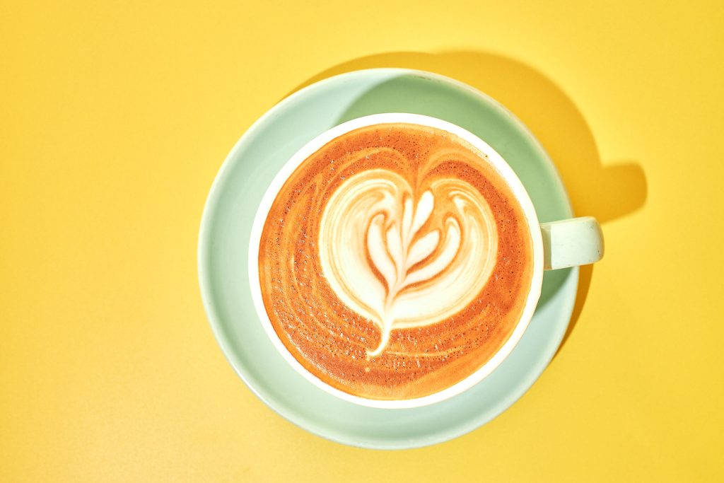 latte art in a mint green cup on a yellow background