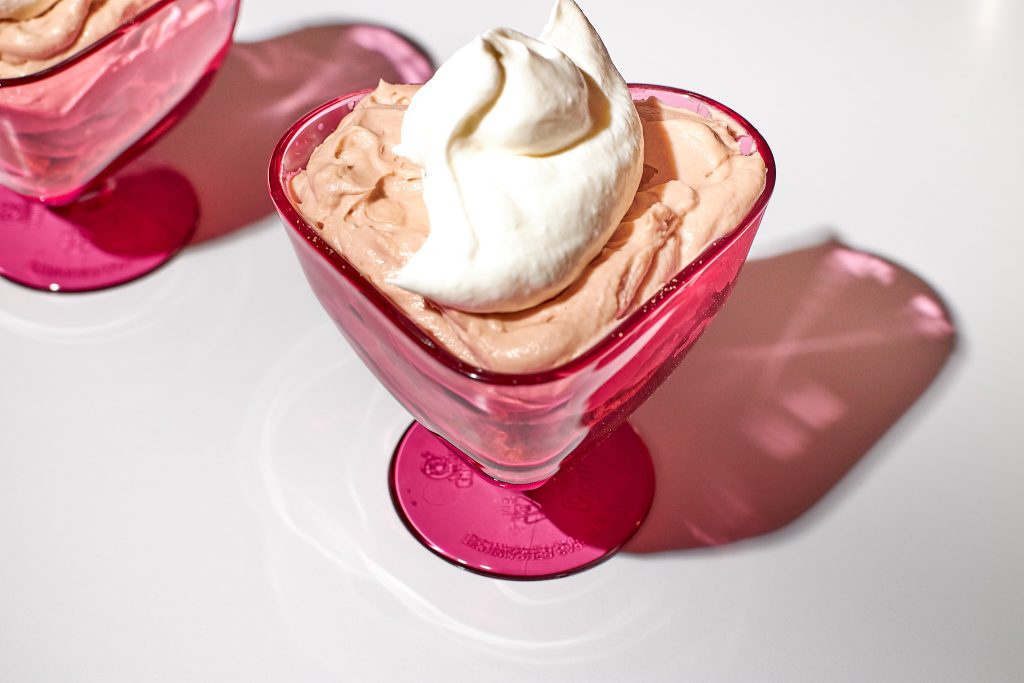 chocolate cheesecake mousse in a heart shaped dessert coupe with whipped cream on top on a white background