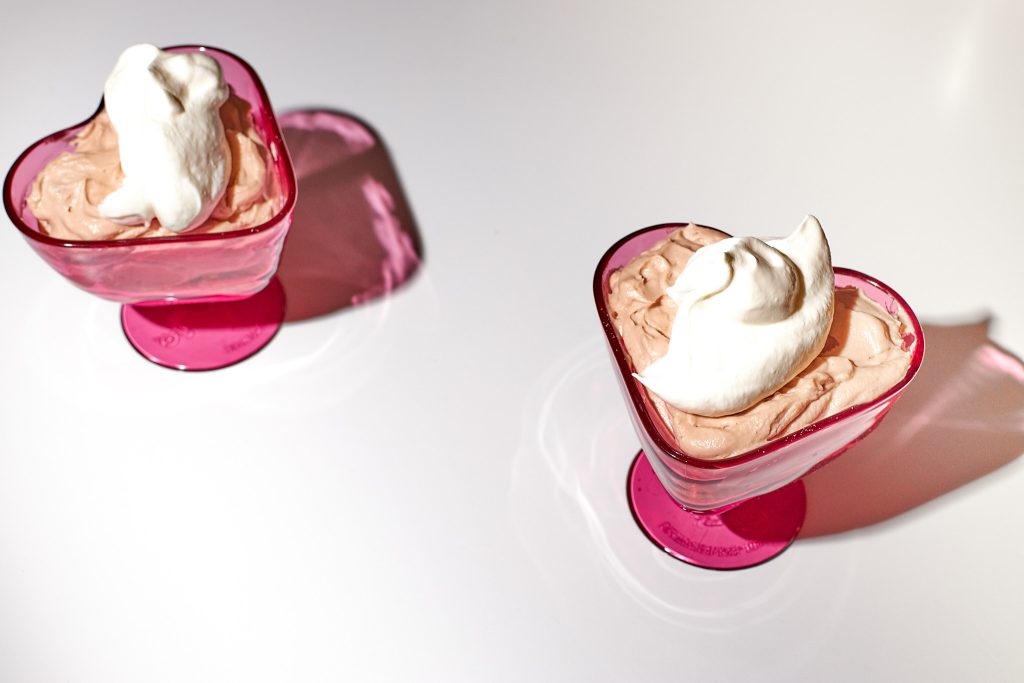 chocolate cheesecake mousse in a heart shaped dessert coupe with whipped cream on top on a white background