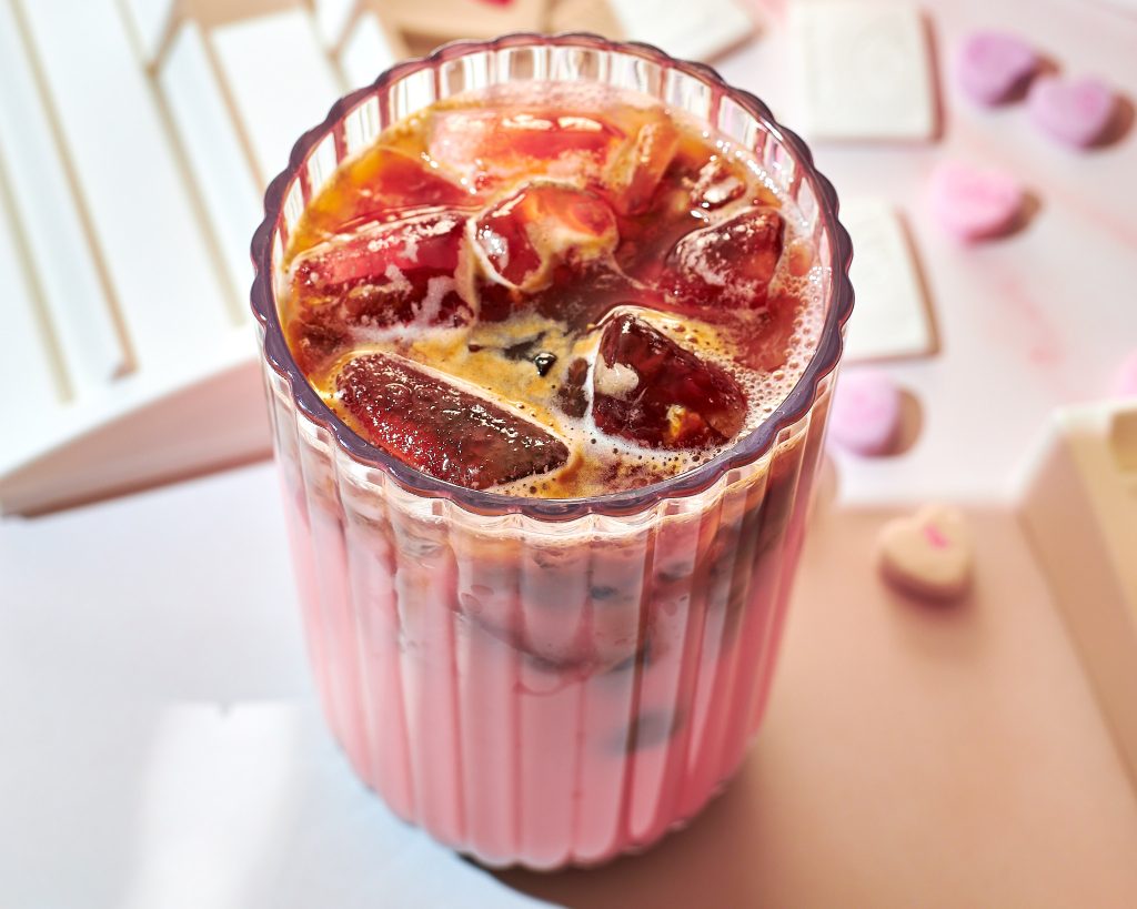 strawberry pink iced latte in a glass on a neutral surface