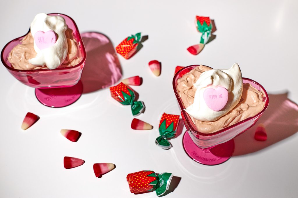 chocolate cheesecake mousse in a heart shaped dessert coupe with whipped cream on top on a white background