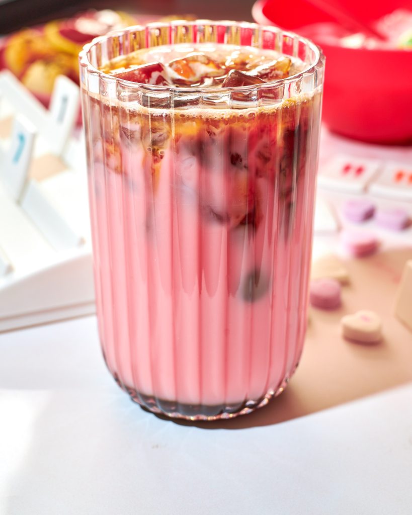 strawberry pink iced latte in a glass on a neutral surface