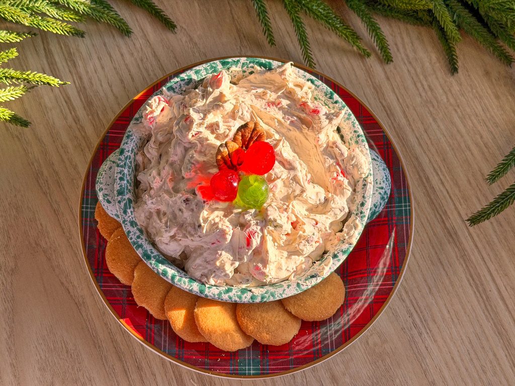 fruit cake dip with red and green cherries on top with nilla wafers on a tartan christmas plate on a neutral background
