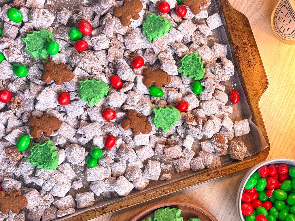 christmas puppy chow with gingerbread men, christmas m&ms and christmas tree shortbread cookies on a kitchen counter with green and red M&Ms in a bowl