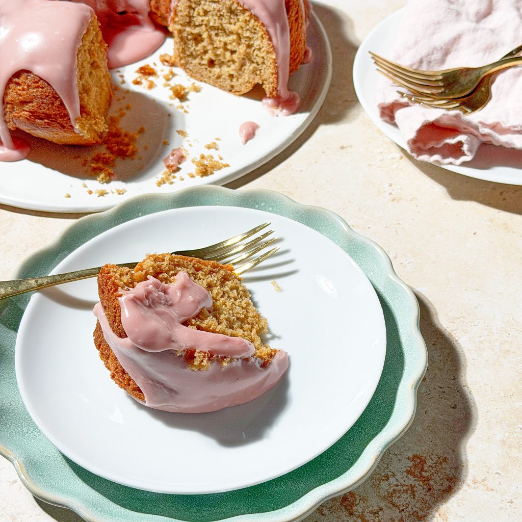 spiced cake with a pink icing on a teal plate with forks on a warm neutral background