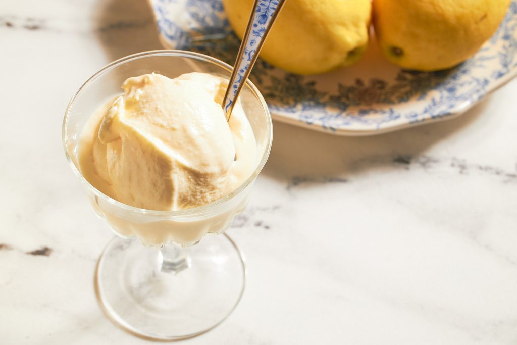yellow ice cream in a glass on a neutral background with real lemon