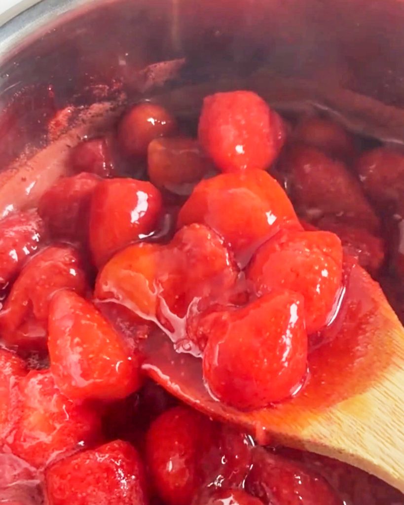 strawberries cooking on the stove with a wooden spoon