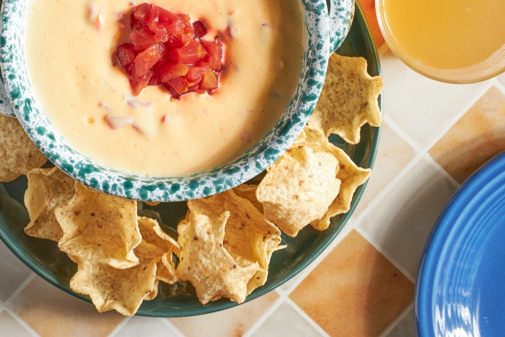 vegan velveeta rotel dip recipe in a green bowl with tortilla chips in the background on a neutral background