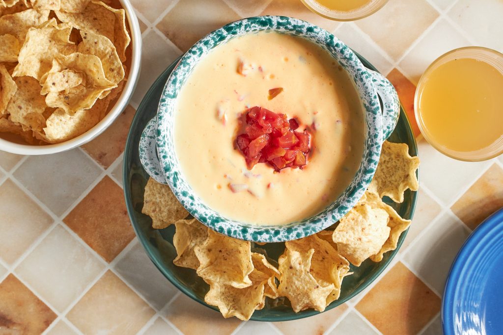 vegan rotel dip in a green bowl with tortilla chips in a white bowl on a neutral background